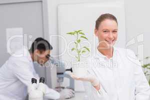 Happy scientist smiling at camera showing plant