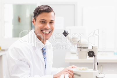 Smiling scientist observing petri dish with microscope