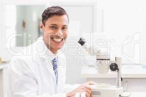 Smiling scientist observing petri dish with microscope