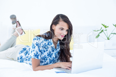 Pretty brunette using her laptop lying on her bed