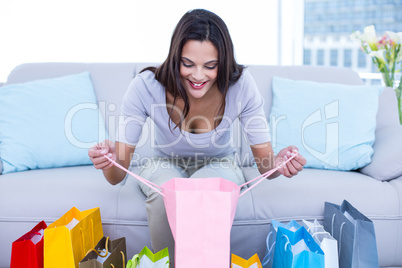 Smiling beautiful brunette sitting on the couch with shopping ba