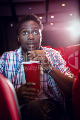 Young man watching a film and drinking soda