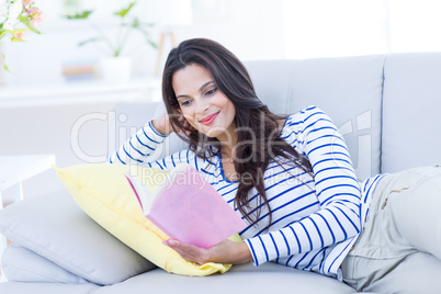 Smiling beautiful brunette relaxing on the couch and reading a b