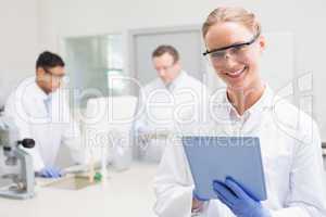 Smiling scientist using tablet while colleagues working behind
