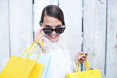 Pretty woman using her smartphone holding shopping bags