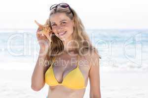 Smiling pretty blonde in bikini holding a starfish and looking a