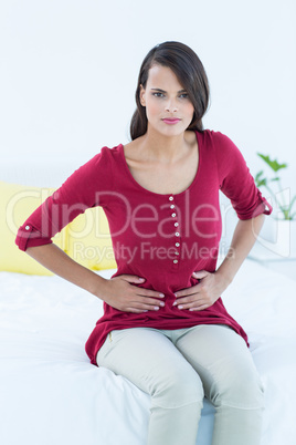 Pretty brunette sitting on bed with stomach pain