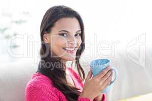 Smiling beautiful brunette relaxing on the couch and holding mug