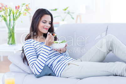 Smiling beautiful brunette relaxing on the couch and eating sala