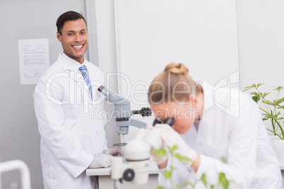 Happy scientist smiling at camera using microscope