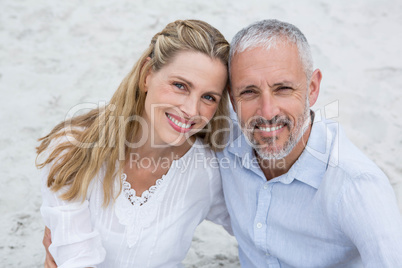 Happy couple sitting on the sand and looking at the camera