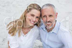 Happy couple sitting on the sand and looking at the camera