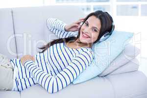 Smiling beautiful brunette relaxing on the couch and listening m
