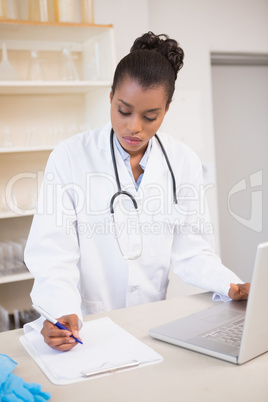 Scientist taking notes while using laptop