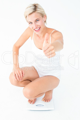 Happy blonde woman crouching on a scales with thumbs up