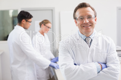 Smiling scientist looking at camera while colleagues working beh