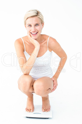 Happy blonde woman crouching on a scales