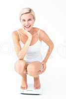 Happy blonde woman crouching on a scales