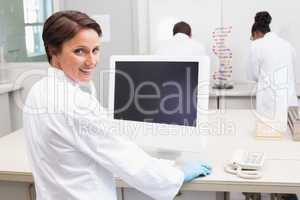 Smiling scientist using computer while colleagues working