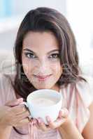 Smiling beautiful brunette relaxing on the couch and holding mug