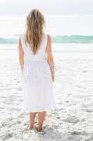 Smiling blonde in white dress standing by the sea
