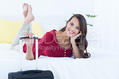 Beautiful woman with a suitcase lying on her bed