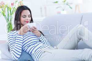 Smiling beautiful brunette relaxing on the couch and holding mug