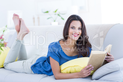 Smiling beautiful brunette relaxing on the couch and reading a b