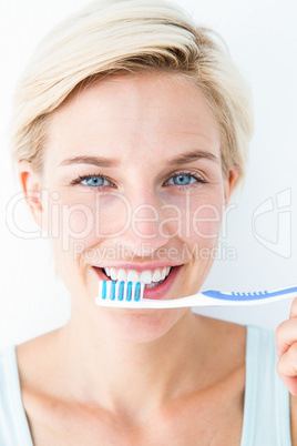 Happy blonde looking at camera holding toothbrush