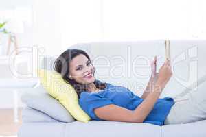 Smiling beautiful brunette relaxing on the couch and reading a b