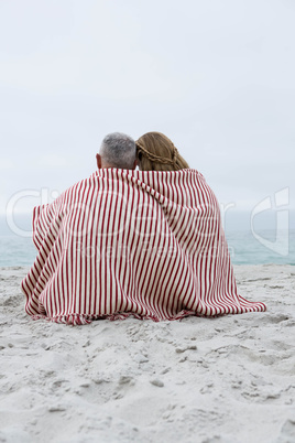 Happy couple sitting on the sand with blanket around them