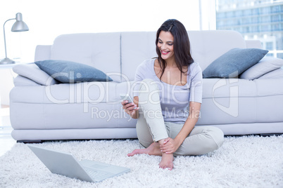 Smiling beautiful brunette sitting on the floor and using her ph