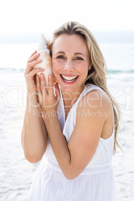 Smiling blonde in white dress listening the seashell