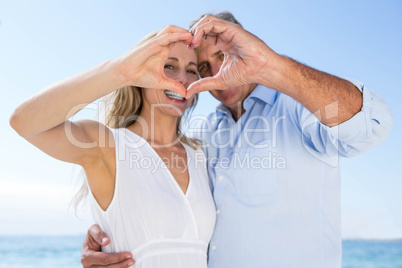 Happy couple smiling at camera and doing heart shape with their