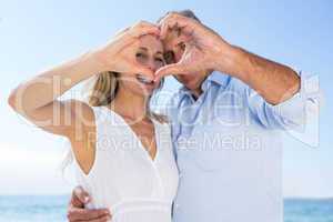 Happy couple smiling at camera and doing heart shape with their