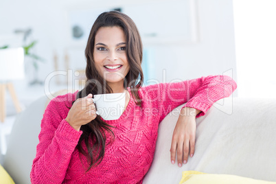 Smiling beautiful brunette relaxing on the couch and holding mug