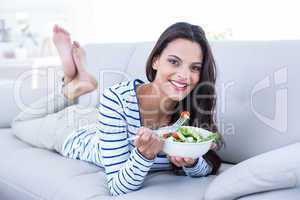 Smiling beautiful brunette relaxing on the couch and eating sala