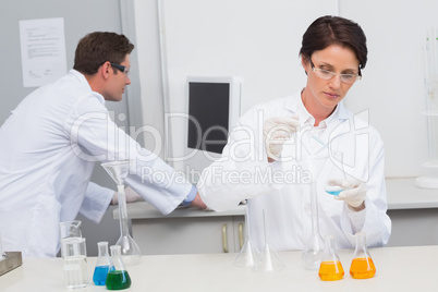 Scientist pouring chemical fluid in funnel and her colleague wor