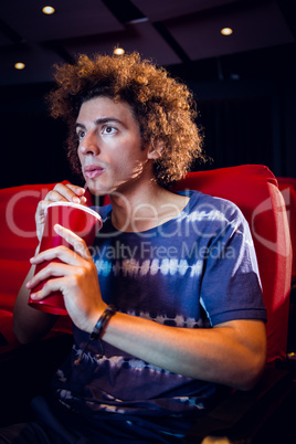 Young man watching a film and drinking soda