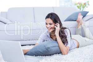 Smiling beautiful brunette lying on the floor and speaking on th