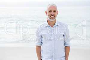 Smiling man standing by the sea hands in pocket