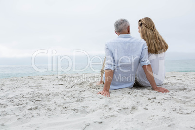 Happy couple sitting on the sand and looking at the sea