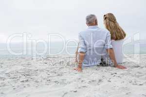 Happy couple sitting on the sand and looking at the sea