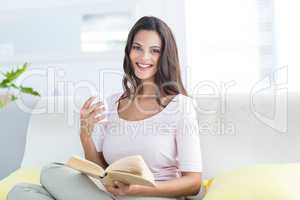 Smiling beautiful brunette holding mug and reading a book while
