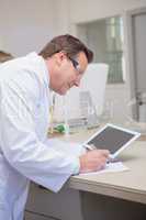 Smiling scientist holding tablet writing on notebook