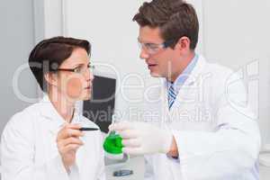 Scientists examining attentively beaker with green fluid