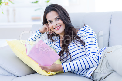 Smiling beautiful brunette relaxing on the couch and reading a b