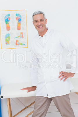 Happy doctor smiling at camera leaning on bed