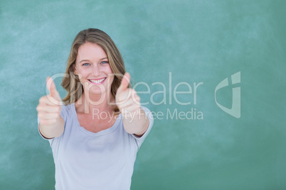 Smiling teacher standing thumbs up in front of blackboard