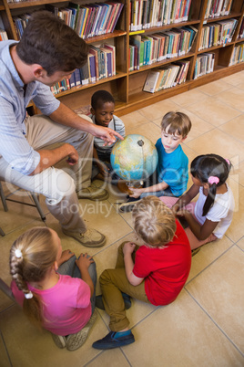 Cute pupils and teacher looking at globe in library